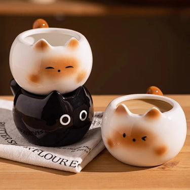 The KittyNook Cat Co. Siamese Cat Coffee Cup sits beside two stacked black and white cat lover mugs on the table.